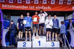 Siegerehrung von Läufern auf dem Podium mit Urkunden vor einer Bühne mit dem Banner „Miteinander ist einfach.“