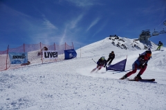 Skirennfahrer auf einer verschneiten Piste bei sonnigem Himmel, kurz vor einer Kurve.