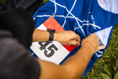 Hände befestigen eine Startnummer 45 an einem blauen Sporttrikot auf Gras.