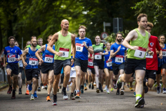 Läufergruppe auf einer Straße, viele mit Startnummern und grünen oder blauen Laufshirts.